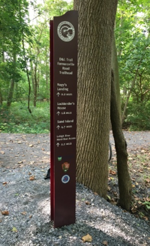 Trailhead sign in a wooded area showing distances to Nagy's Landing, Locktender's House, and Sand Island along the D&L Trail.